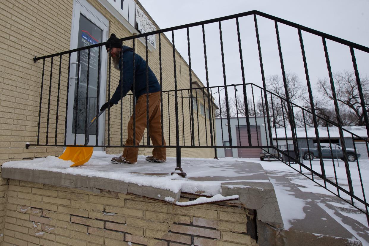 Shawn Holthaus, an employee with A-1 Plumbing, helps to scrape snow and ice away late Thursday morning just outside a building at 110 N.E. Lyman Road.