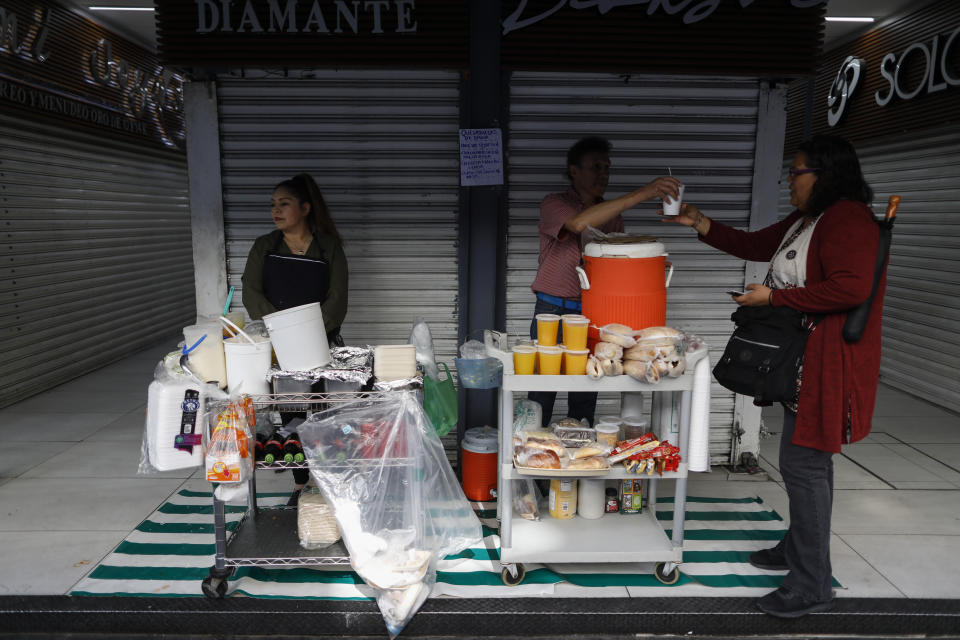 Workers from the Oasis Restaurant serve up breakfast from street-side carts, a pre-existing system that they say customers are increasingly choosing over inside seating as coronavirus worries grow, in central Mexico City, Tuesday, March 24, 2020. Beginning Monday, Mexico's capital shut down museums, bars, gyms, churches, theaters, and other non-essential businesses that gather large numbers of people, in an attempt to slow the spread of the new coronavirus. (AP Photo/Rebecca Blackwell)