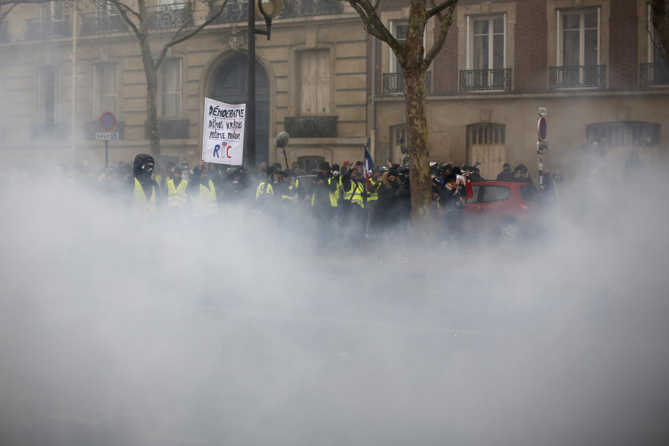 Yellow vest demonstrators stand behind tear gas after a march Saturday, Jan. 19, 2019 in Paris. Thousands of yellow vest protesters rallied in several French cities for a tenth consecutive weekend on Saturday, despite a national debate launched this week by President Emmanuel Macron aimed at assuaging their anger. (AP Photo/Thibault Camus)