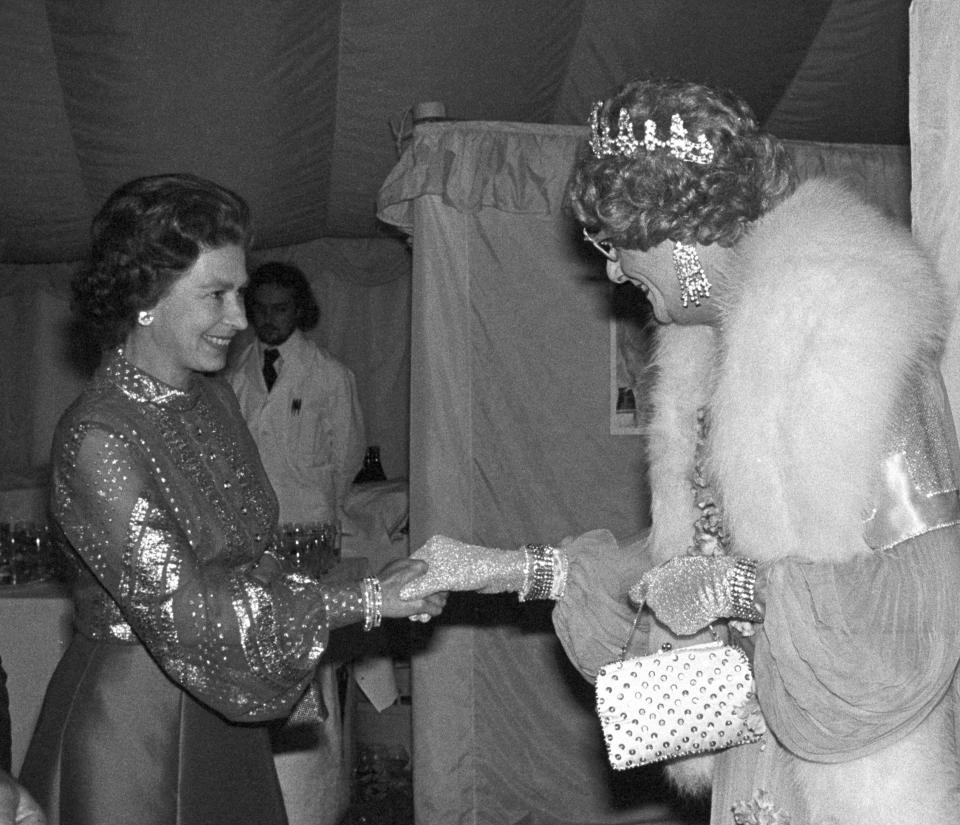 FILE - Britain's Queen Elizabeth II, left, shakes hands with Barry Humphries as Dame Edna Everage after a gala variety performance, in Windsor, England, May 29, 1977. Tony Award-winning comedian Barry Humphries, internationally renowned for his garish stage persona Dame Edna Everage, a condescending and imperfectly-veiled snob whose evolving character has delighted audiences over seven decades has died on Saturday, April 22, 2023, after spending several days in a Sydney hospital with complications following hip surgery, a Sydney hospital said. (PA via AP, File)