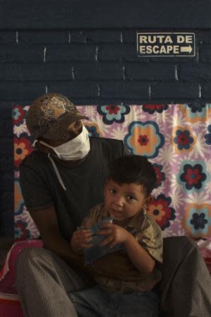 A child is embraced by his father who covers his face with a mask, for protection from the ashes spewed by the Chaparrastique volcano, at a school being used as a shelter in the municipality of San Miguel December 30, 2013. REUTERS/Ulises Rodriguez