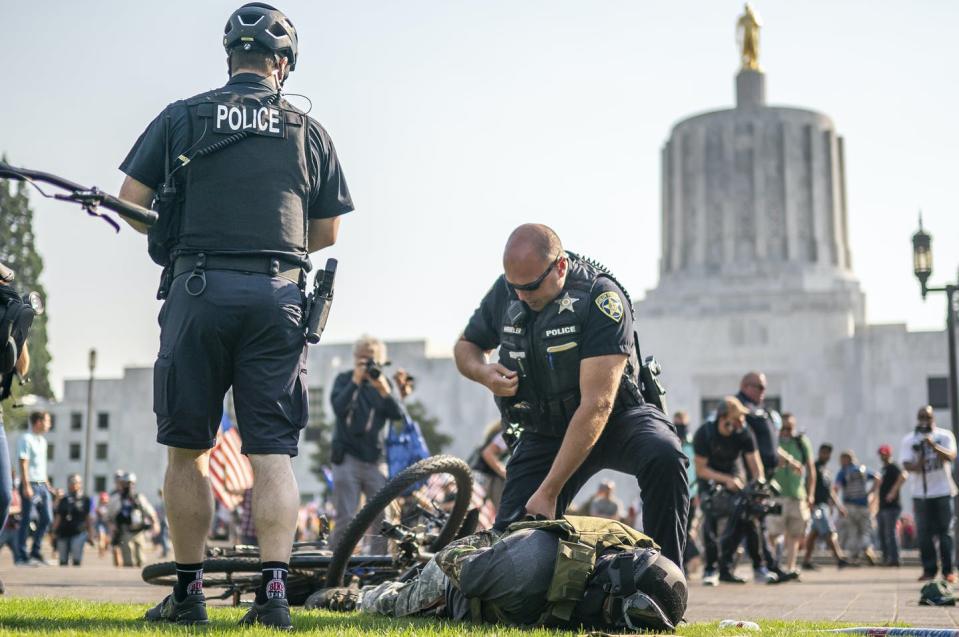 Man in militia gear lies face down on the ground in handcuffs with police standing over