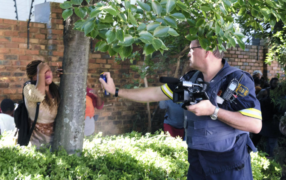 A South African Police officer pepper sprays a woman, at the United Nations High Commissioner for Refugees (UNHCR) compound in Pretoria, South Africa, Friday, Nov. 15, 2019. Police in South Africa removed about 150 refugees who the United Nations refugee agency says forced their way into its compound while protesting recent anti-immigrant attacks. (AP Photo/Elna Schütz)