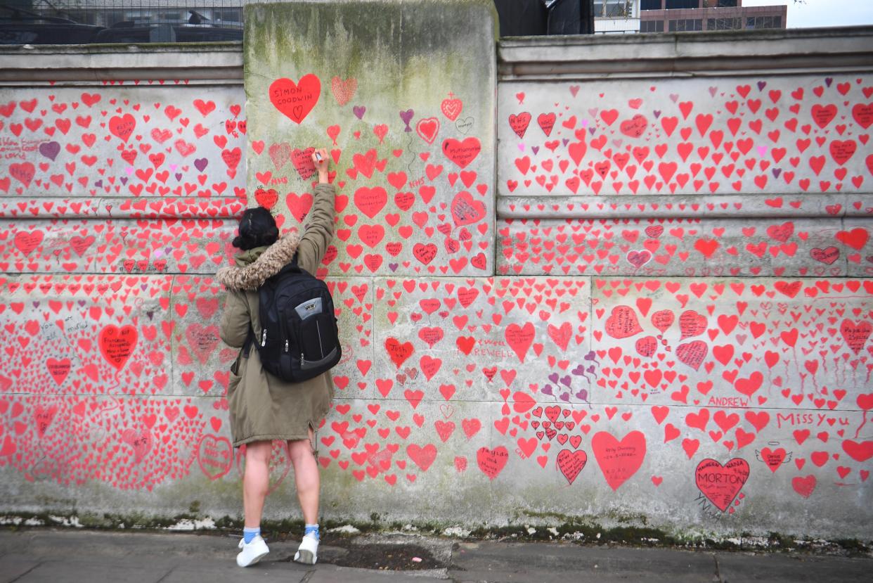 A woman writes in a heart on the National Covid Memorial Wall on the Embankment in London (Victoria Jones/PA) (PA Wire)