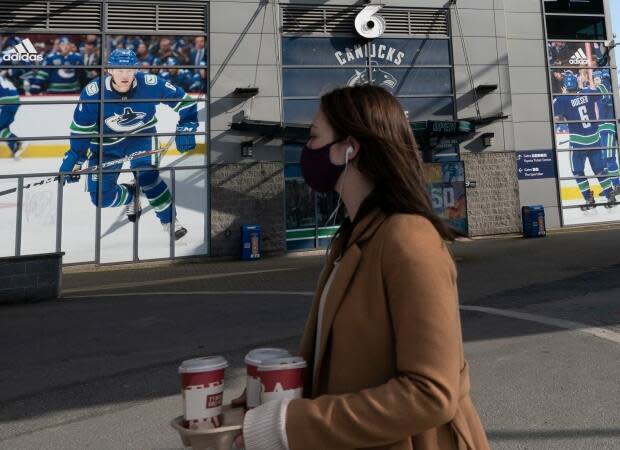 A woman wearing a protective face covering walks past Rogers Arena in downtown Vancouver. A total of 26 Canucks players and coaches tested positive during the COVID-19 outbreak that involved a variant of the virus.