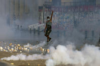 An anti-government protester flashes the victory sign amid tear gas fired by riot police during a protest marking the first anniversary of the massive blast at Beirut's port, near Parliament Square, In Beirut, Lebanon, Wednesday, Aug. 4, 2021. United in grief and anger, families of the victims and other Lebanese came out into the streets of Beirut on Wednesday to demand accountability as banks, businesses and government offices shuttered to mark one year since the horrific explosion. (AP Photo/Bilal Hussein)