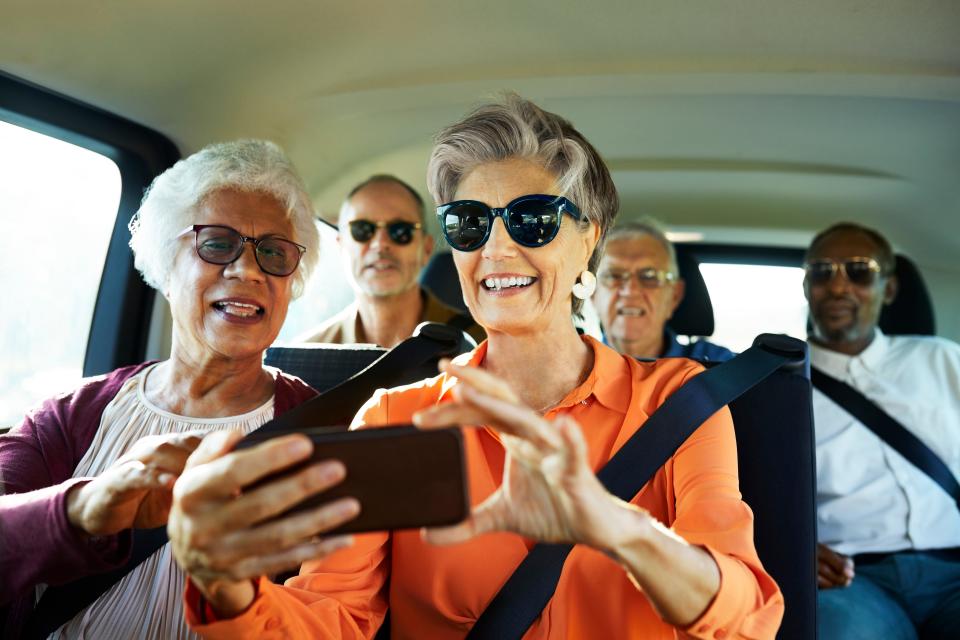 Smiling woman using smart phone by friend in car. Males and females are traveling together during wine tour.