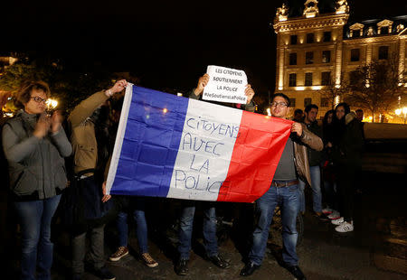 People hold up a national flag which reads, "Citizens with the police", as they take part with police officers in an unauthorised protest against anti-police violence in front of the Police Prefecture in Paris, France, October 21, 2016. REUTERS/Jacky Naegelen