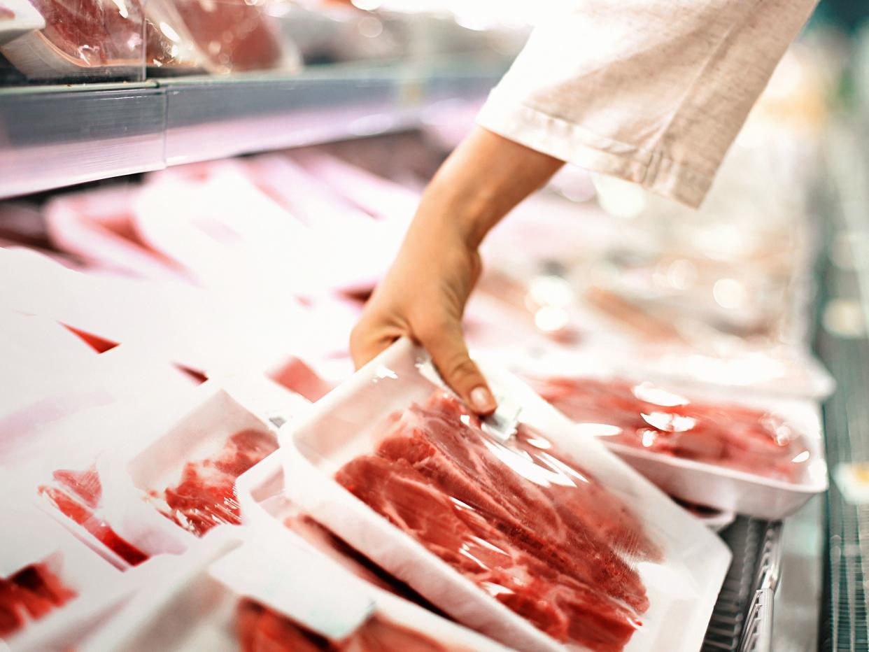 Closeup side view of a woman choosing some fresh meat at local supermarket. The meat is cut into chops and packed into one pound packages. She has reached for a package of beef sirloin steaks.