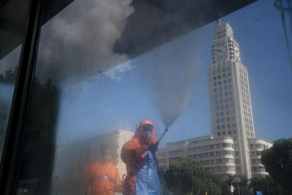 A city worker sprays disinfectant at a bus stop in Rio de Janeiro, Brazil, Tuesday, March 24, 2020, to help prevent the spread of the new coronavirus. The tower behind is the central train station. (AP Photo/Leo Correa)