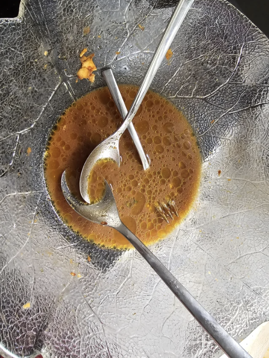 An empty bowl with three spoons resting crossed over leftover soup with floating oil, on a textured surface