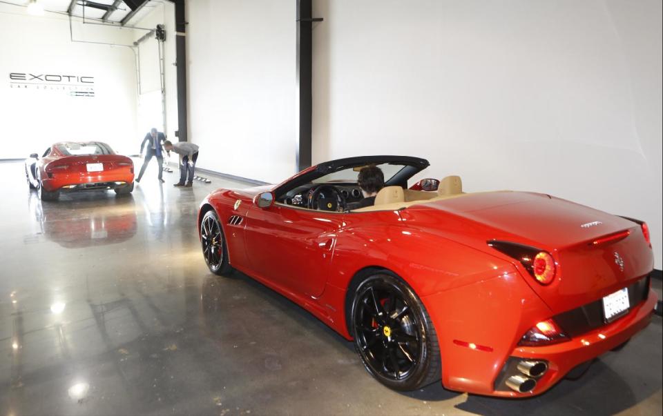 In this Wednesday, March, 26, 2014 photo, Douglas Sawyer, 23, top right, rents out a 2013 Dodge Viper, left, while his friend, Michael Clark, 22, sits inside a 2014 Ferrari California at the Enterprise Exotic Car Collection showroom near Los Angeles International Airport. (AP Photo/Damian Dovarganes)