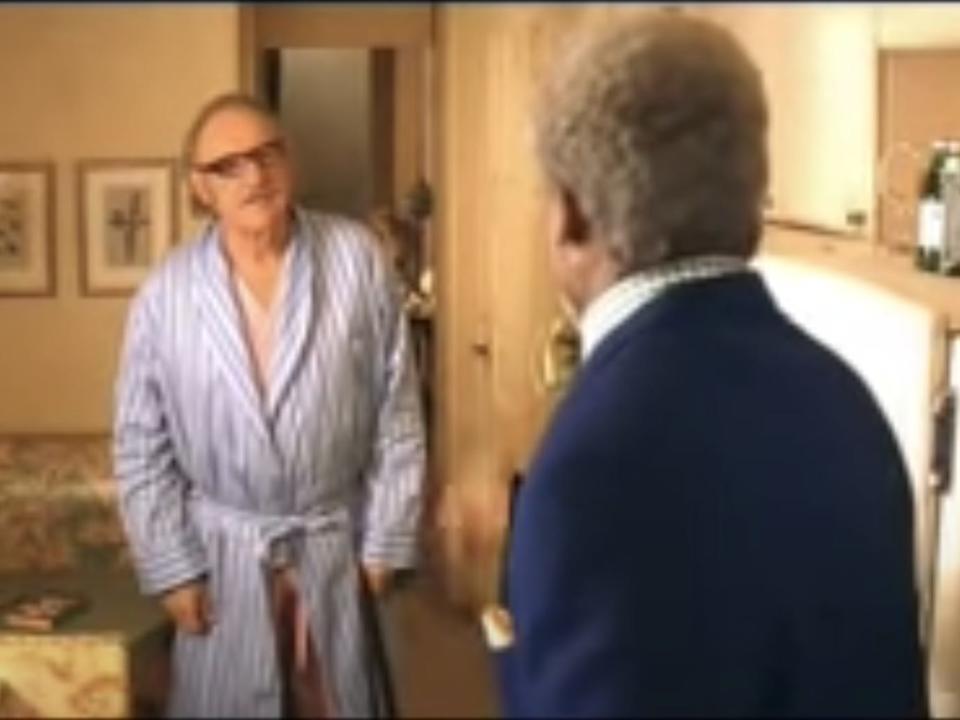 Royal Tenenbaum (Gene Hackman) stands in a bathrobe in the family's kitchen while arguing with Henry (Danny Glover), who has his back to the viewer.