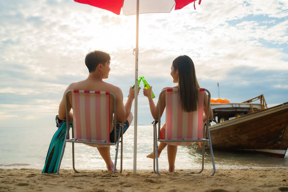 A couple relaxing on the beach and drinking beer during their holiday.