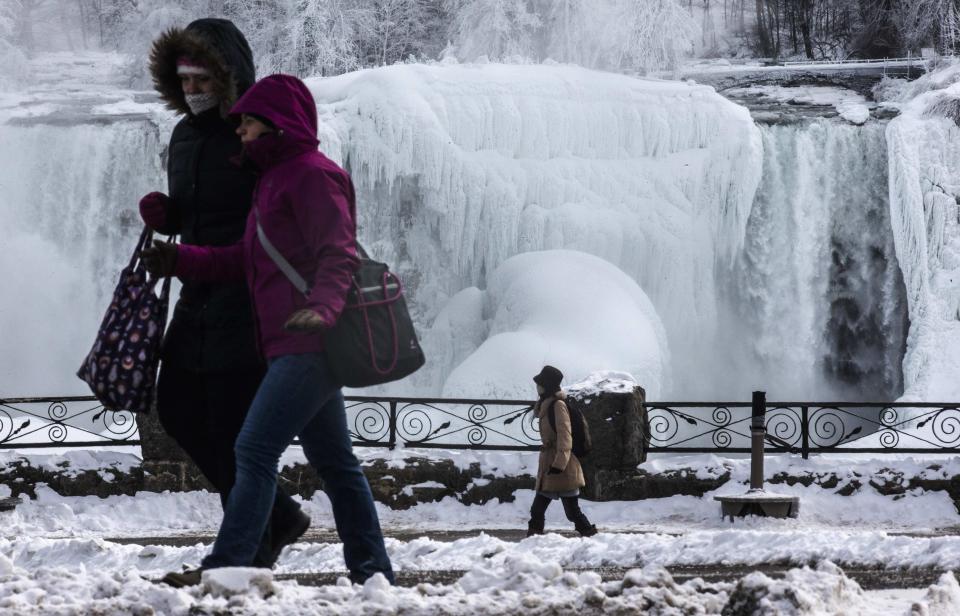 People walk in front partially frozen American side of the Niagara Falls on during sub-freezing temperatures in Niagara Falls, Ontario March 3, 2014. REUTERS/Mark Blinch