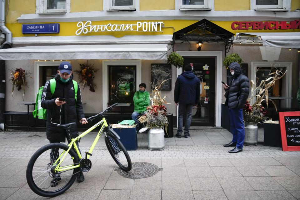 Food delivery couriers wait to get takeaway food to deliver to customers in front of a cafe, which is closed due to coronavirus in Moscow, Russia, Friday, Oct. 29, 2021. Russia on Friday recorded another record of daily coronavirus deaths as authorities hoped to stem contagion by keeping most people off work. Moscow introduced the measure starting from Thursday, shutting kindergartens, schools, gyms, entertainment venues and most stores, and restricting restaurants and cafes to only takeout or delivery. (AP Photo/Alexander Zemlianichenko)