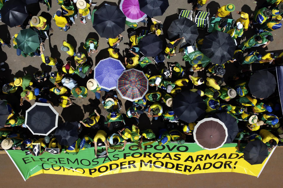 FILE - Supporters of Brazilian President Jair Bolsonaro stand behind a banner that reads in Portuguese; "We, the people, elect the Armed Forces as a moderating power", in a protest against Bolsonaro's run-off election loss, outside Army headquarters in Brasilia, Brazil, Nov. 15, 2022. For months, the high command permitted pro-Bolsonaro campsites supportive of military intervention outside their barracks.(AP Photo/Eraldo Peres, File)