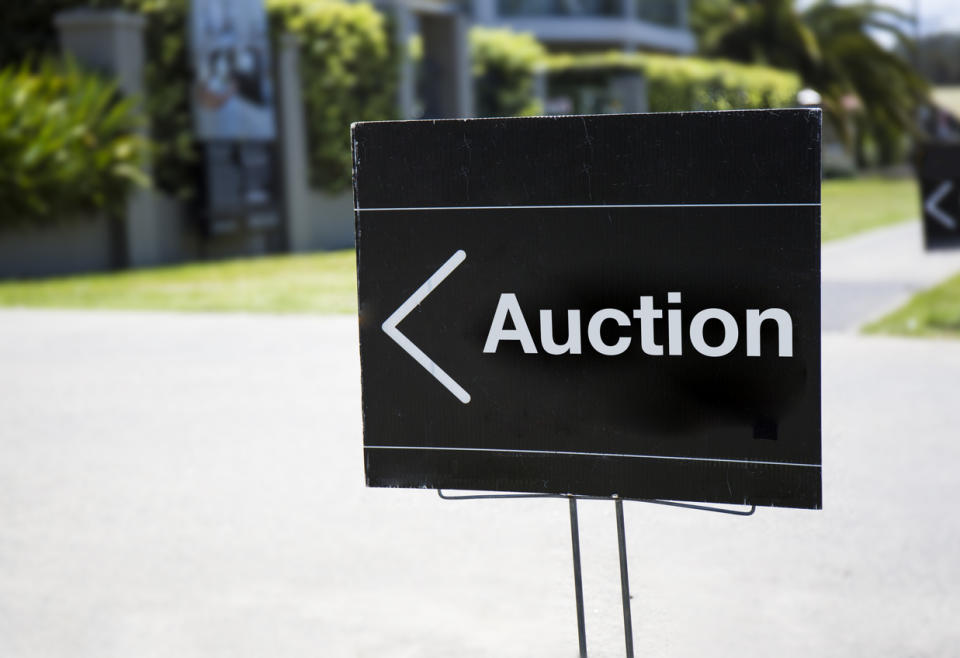 A-black-and-white-sign-with-the-word-Auction-sits-along-a-street-in-a-treed-neighborhood.