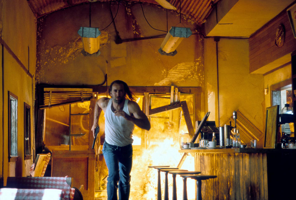 Nicolas Cage running through a burning building while holding onto a gun in a scene from the film 'Con Air', 1997. (Photo by Touchstone Pictures/Getty Images)