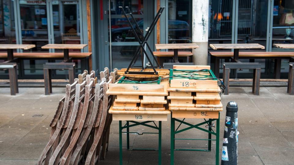 Zusammengestellte Tische und aufgestapelte Stühle stehenvor einem geschlossenen Café in Hamburg.