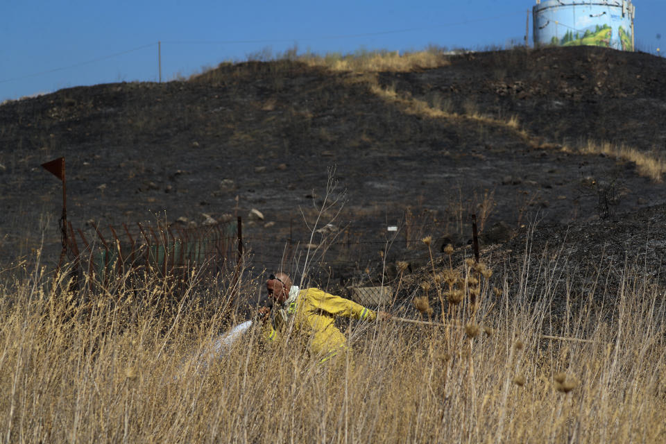 An Israeli firefighter attempts to extinguish a fire caused by rocket fired from Lebanon into Israeli territory near the northern Israeli town of Kiryat Shmona, Wednesday, Aug. 4, 2021. Three rockets were fired from Lebanon into Israeli territory Wednesday and the army fired back, Israel's military said. There was no immediate information on damages or casualties. (AP Photo/Ariel Schalit)