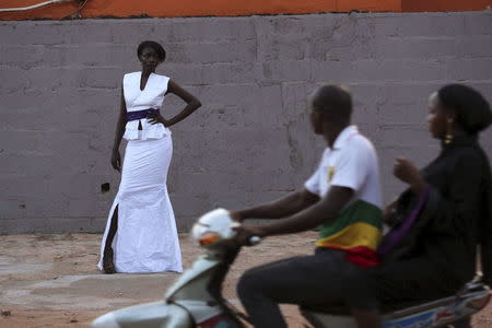 People on a motorcycle ride past model Atou Cisse wearing a bazin outfit made by designer Mariah Bocoum Keita in Bamako, Mali, October 21, 2015. REUTERS/Joe Penney