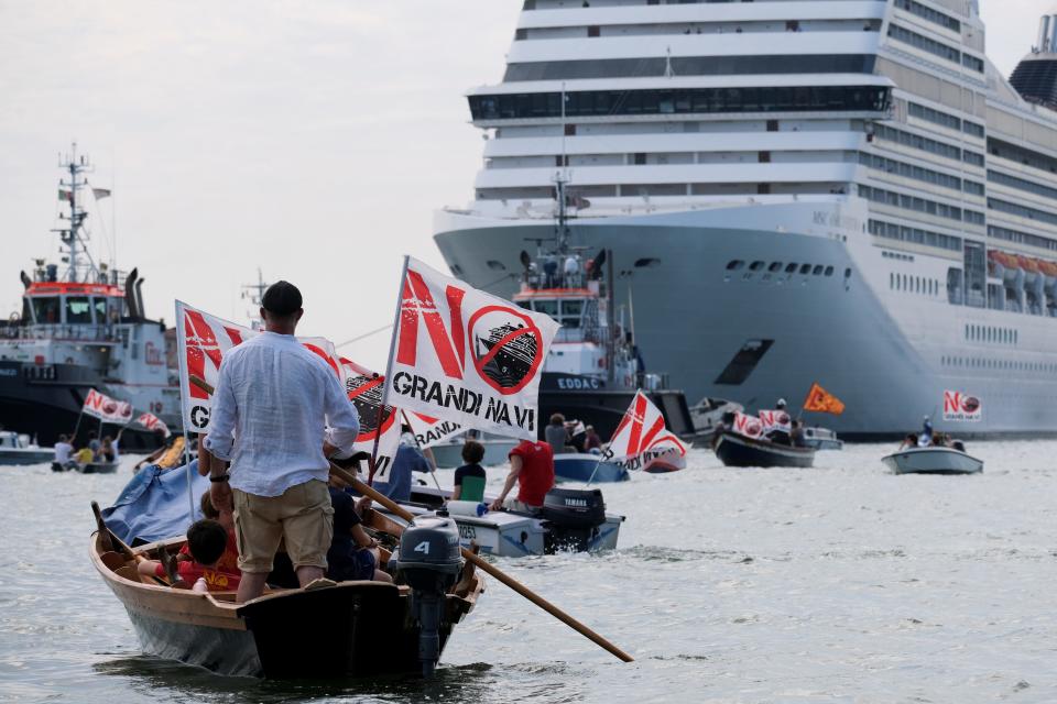 This image shows people on small boats with signs that say "NO" headed towards a large cruiseship