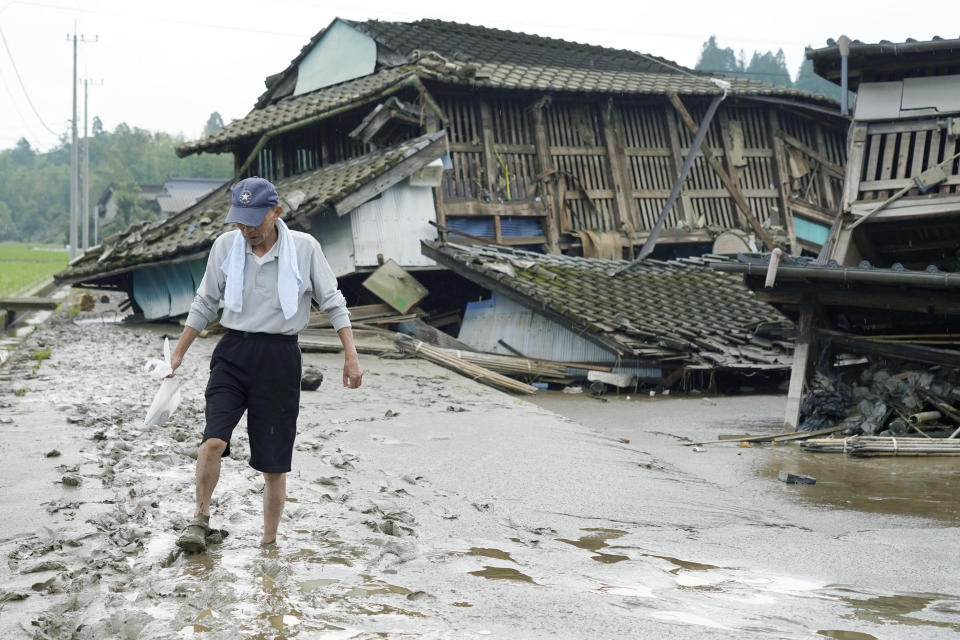 A man walks on muddy road past houses damaged by flood in Kuma village, Kumamoto prefecture, southwestern Japan, Sunday, July 5, 2020. Heavy rain in Kumamoto has triggered flooding and mudslides Saturday and left dozens still being stranded at their homes and other facilities. (Koji Harada/Kyodo News via AP)