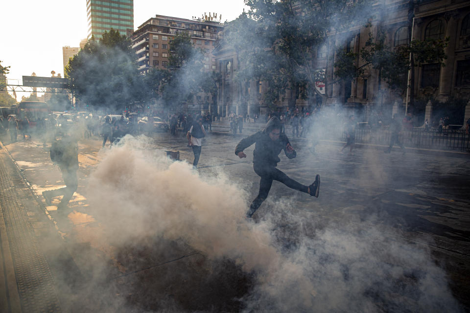 A protester kicks a tear gas canister launched by police near the Santa Lucia subway station during a protest against the rising cost of subway and bus fares, in Santiago, Friday, Oct. 18, 2019. (AP Photo/Esteban Felix)