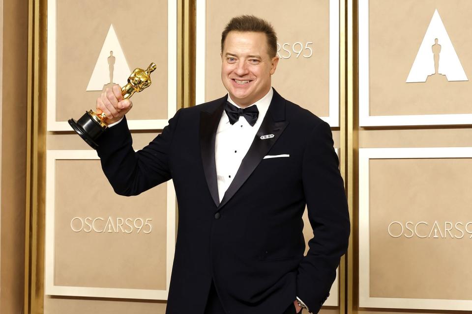 brendan fraser raising his academy award statuette with his right arm and smiling