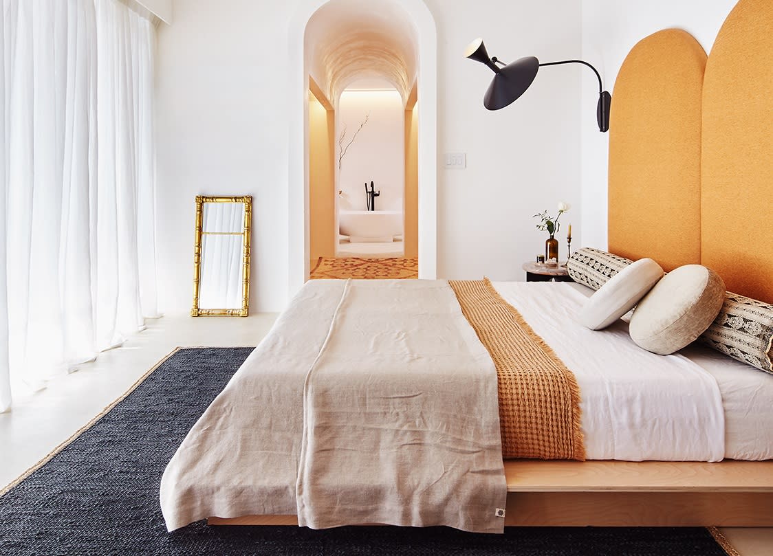  A bedroom with white walls and yellow accents facing a large floor to ceiling window with a voile curtian. 