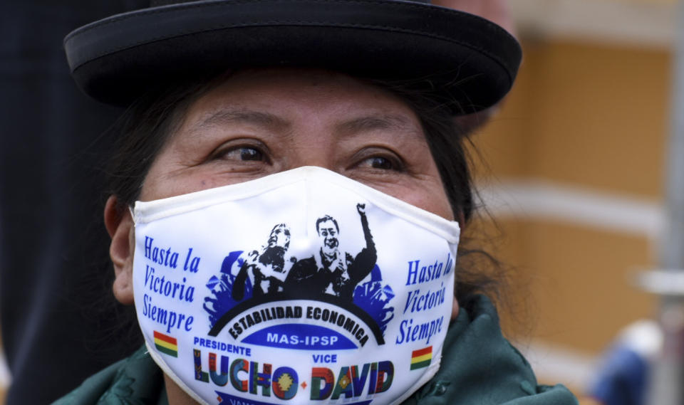 A woman wearing a mask amid the coronavirus pandemic with the image Bolivia's new President Luis Arce and Vice President David Choquehuanca stand at Plaza Murillo during their inauguration in La Paz, Bolivia, Sunday, Nov. 8, 2020. (AP Photo/Sara Aliaga)