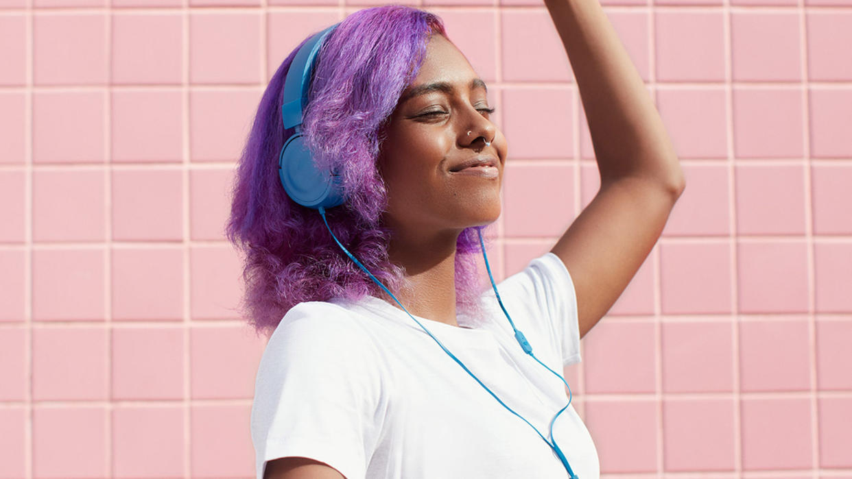  A women wearing blue headphones against a pink tiled wall. 