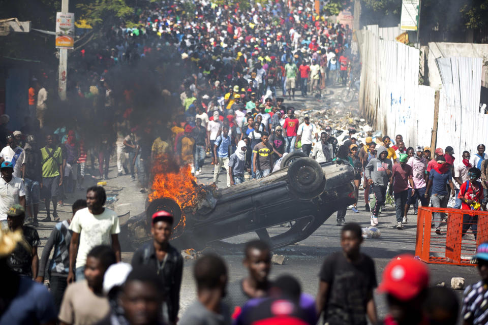 CORRECTS ARREST DATE - FILE - In this Feb. 12, 2019 file photo, an overturned car burns during a protest demanding the resignation of Haitian President Jovenel Moise in Port-au-Prince, Haiti. The Feb. 17, 2019 arrest of a group of armed contractors’, their unexplained release and the still-murky nature of their mission have helped fuel political chaos in Haiti, where Moise has faced months of protests over his government’s failure to prosecute the theft and mismanagement of $2 billion in subsidized oil aid from Venezuela under the administration of his predecessor and political patron, Michel Martelly. (AP Photo/Dieu Nalio Chery, File)