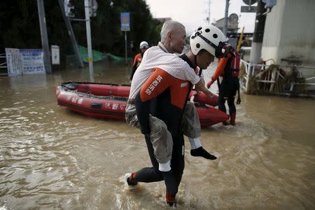 An elderly man is rescued by a firefighter at a residential area flooded by the Kinugawa river, caused by typhoon Etau in Joso, Ibaraki prefecture, Japan, September 11, 2015. REUTERS/Issei Kato