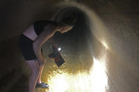 Activist Juniper Simonis examines a culvert near the Willamette River where Simonis has found crowd control agents that have come down stormwater drains from nearby protest sites in Portland, Ore., on Oct. 2, 2020. Night after night in Portland, tear gas and other crowd control devices enveloped protesters and bystanders in aerosolized compounds that then settled on the ground and wound up washed into storm drains. Test samples from those storm drains have turned up heavy metals and chemicals at much higher levels than samples collected from control sites elsewhere. (AP Photo/Andrew Selsky)