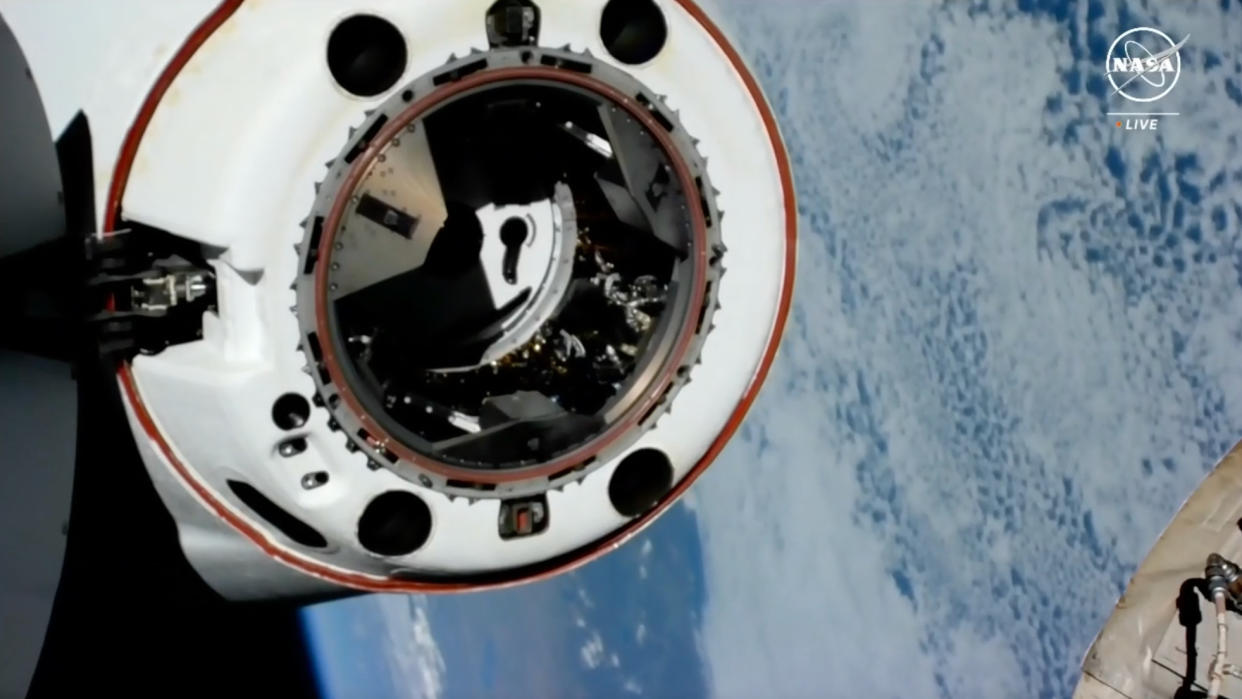  A white spacecraft undocks from the international space station with earth in the background. 