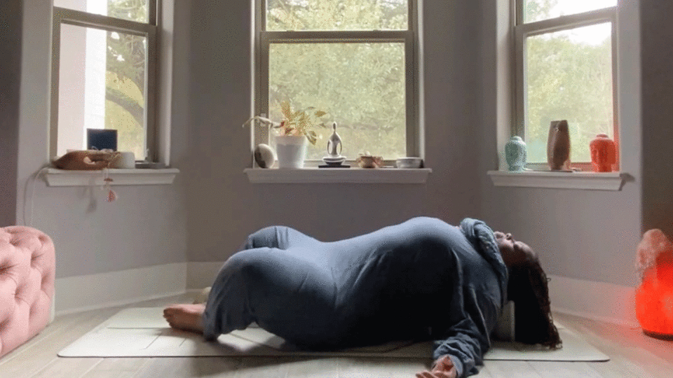 Woman stretching her chest and hips in a reclining yoga stretch in her bedroom