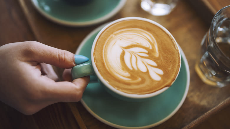 Person holding a latte in a blue mug