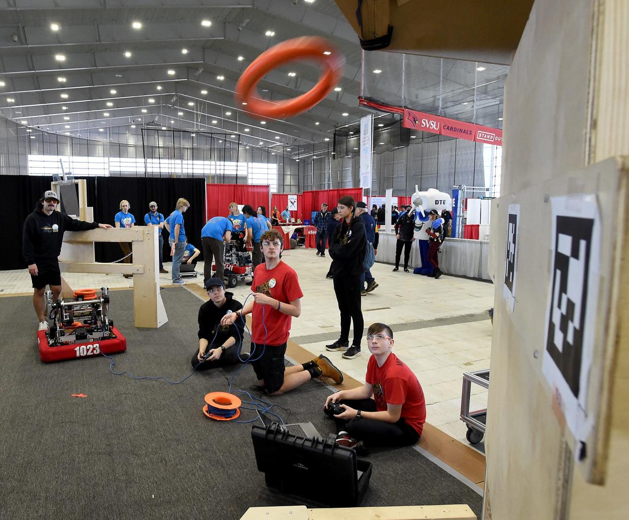 Ethan Bellino drive team coach (back left) watches the high school Bedford Express FRC Team #1023 robotics team members electronic lead and chassis driver Eric Koenemann, CAD lead Walker Schmus, drive team manipulator Ryan Marckel and looking on drive team technician Olivia Szczepanik practice the Crescendo High Note Toss on the practice field at the FIRST in Michigan State Championship 2024 at Saginaw Valley State University April 5, 2024.