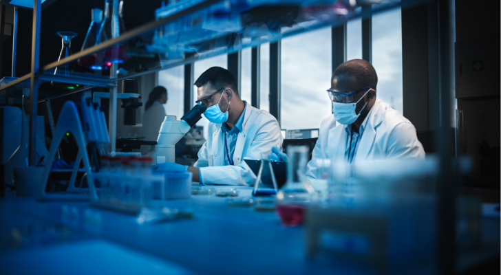 Modern Medical Research Laboratory: Two Scientists Wearing Face Masks use Microscope, Analyse Sample in Petri Dish, Talk. Advanced Scientific Lab for Medicine, Biotechnology. Blue Color. KZR stock.