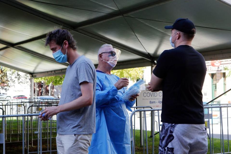 Two men with face masks stand near a medical worker at a Covid-19 testing centre in Perth.