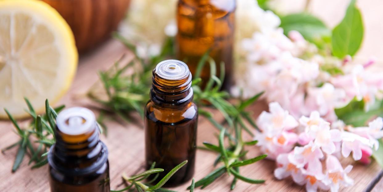 bottles of essential oil with herbs and fruits on wooden table rosemary, lemon and flowers