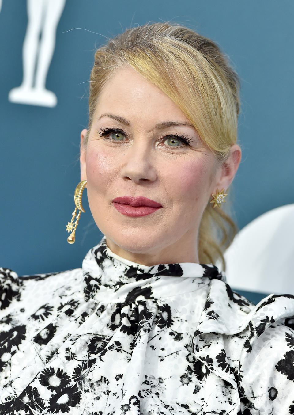 Christina Applegate wearing a patterned blouse with ruffled collar and gold earrings