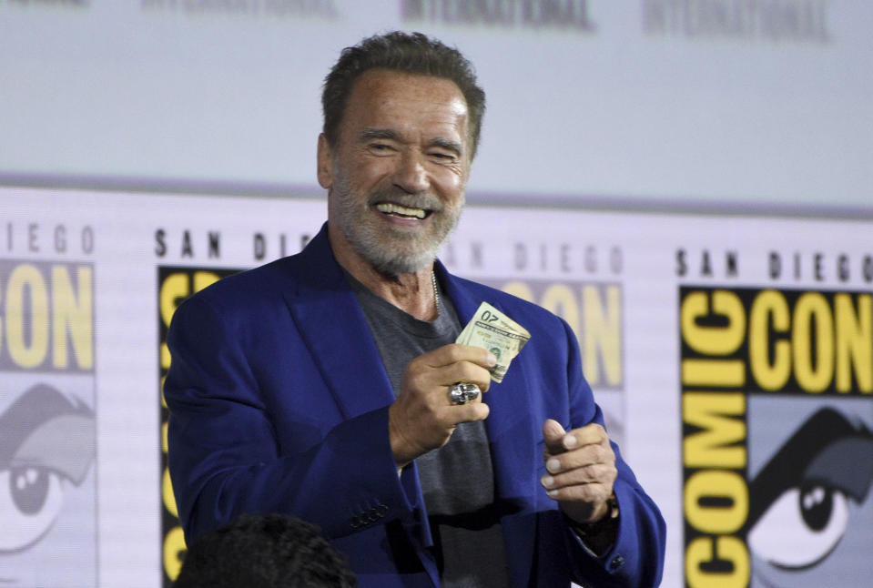 Arnold Schwarzenegger gets twenty dollars after winning a bet to fellow cast member Diego Boneta at the "Terminator: Dark Fate" panel on day one of Comic-Con International on Thursday, July 18, 2019, in San Diego. (Photo by Chris Pizzello/Invision/AP)