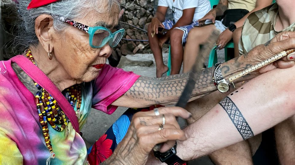 Whang-Od hammers away on a visitor's arm. - Kathleen Magramo/CNN