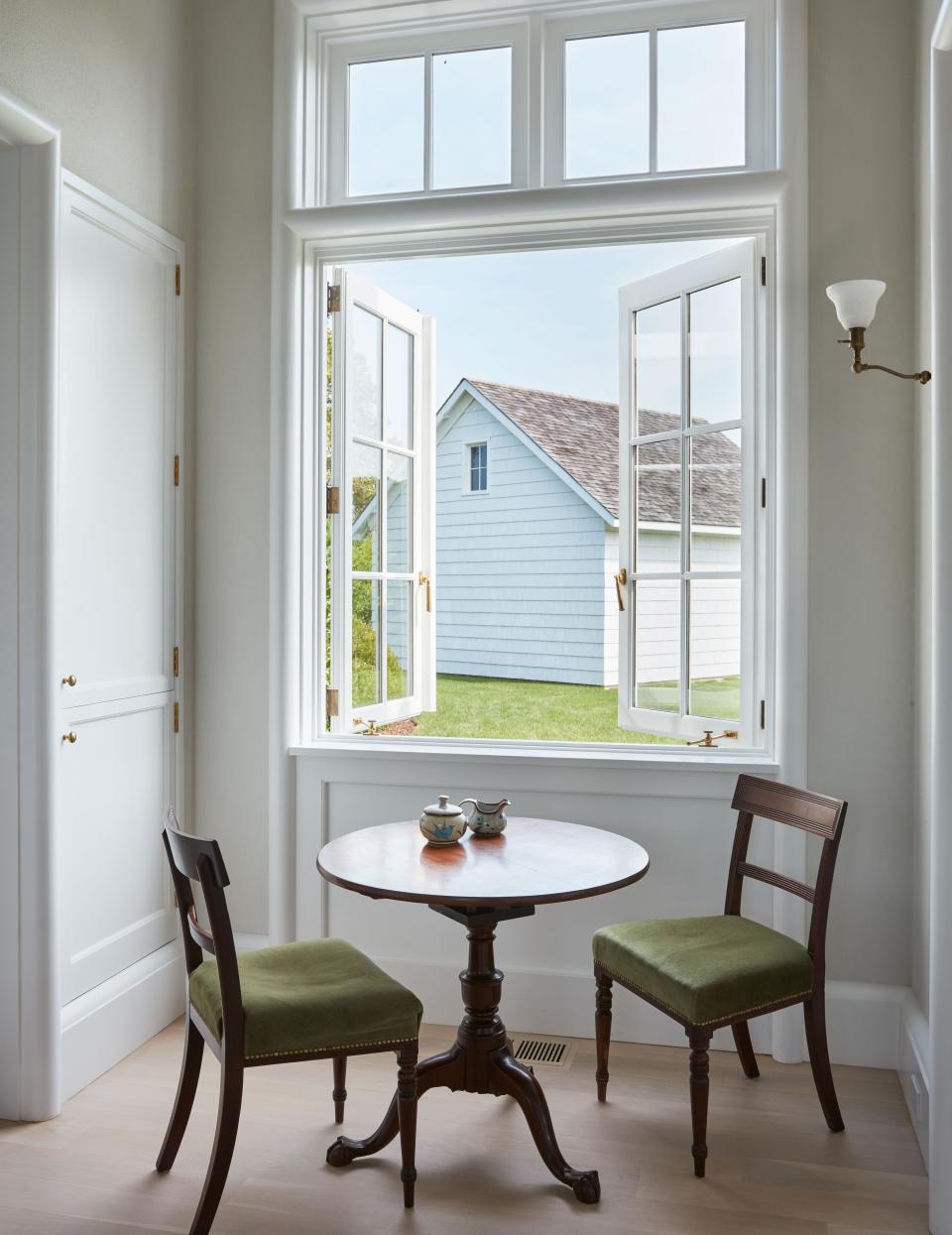 A pair of velvet-upholstered regency chairs and a Queen Anne table stand at the kitchen window.
