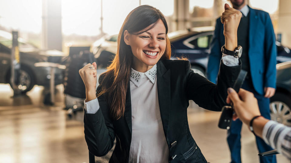 Cheerful young woman receiving the keys of her new car at car dealership.