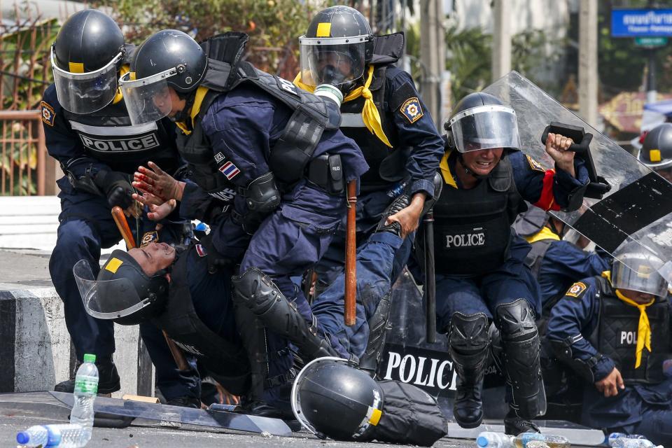 Thai riot police officers assist a colleague during clashes with anti-government protesters near Government House in Bangkok