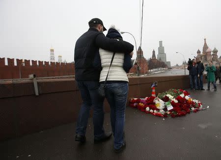 A man comforts a woman as they visit the site where Boris Nemtsov was recently murdered, with St. Basil's Cathedral and the Kremlin seen in the background, in central Moscow, February 28, 2015. REUTERS/Sergei Karpukhin